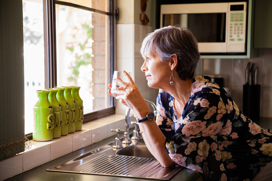 Mature woman holding glass of water kin kitchen looking away