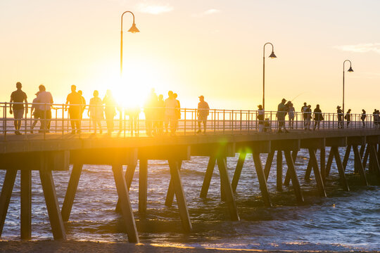 Silhouettes of a crowd of people walking on an ocean jetty at sunset