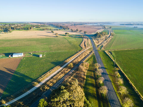An aerial view of roads and a railway line intersecting through green farmland