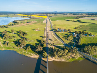 Aerial view of railway line and a country road converging as they cross a river