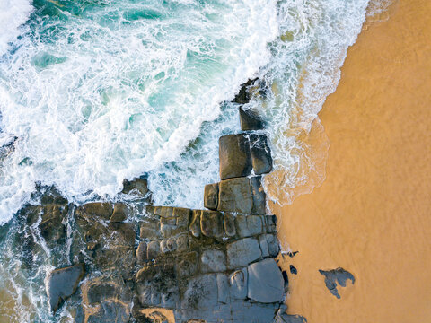 Looking down on waves crashing over rocks on a beach