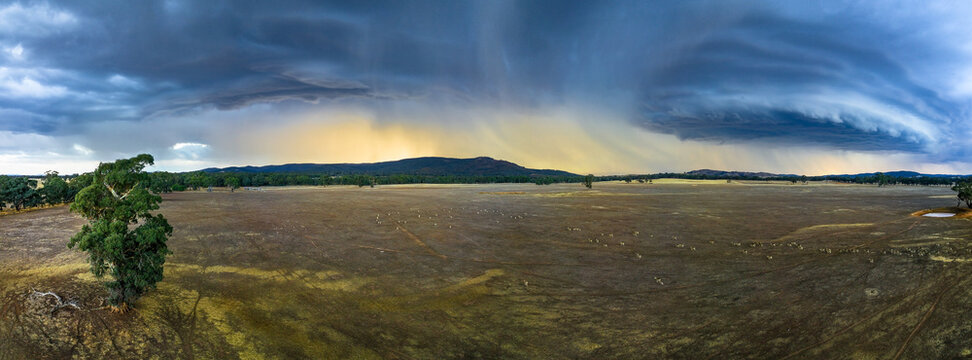 A large storm front over dry farmland and hill at sunset.