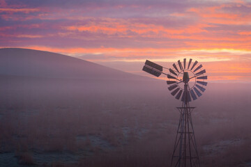 A windmill at the base of a hill in fog at sunrise