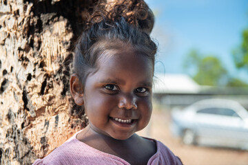 Aboriginal 3 year old girl smiling by a tree