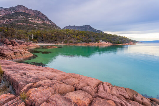 A rocky shoreline around a calm bay at the base of a mountain range