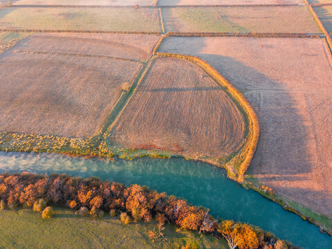 Aerial view of farmland and autumn trees on the banks of a river