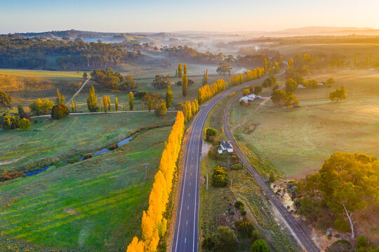 Aerial view of a country road winding through autumn trees at sunrise