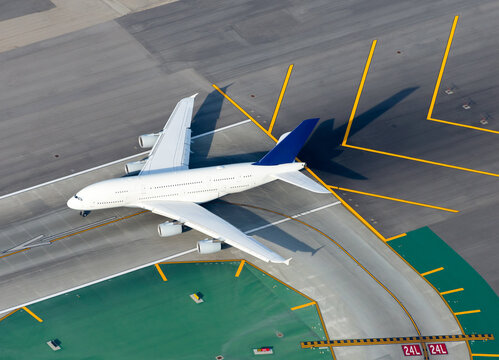 Aerial view of large white unidentified aircraft in an international airport runway before take off. Runway and taxiway signs. Airplane near yellow chevrons.