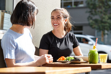 Female friends sitting outdoors at cafe in sunshine