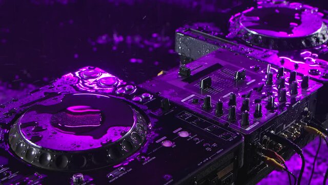 Audio mixing controller stands in a dark studio with purple illumination. DJ tools in the pouring rain. Top view. Close up. Slow motion.