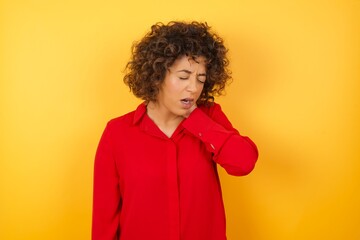 Young arab woman with curly hair wearing red shirt  on yellow background Suffering of neck ache injury, touching neck with hand, muscular pain