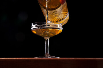 Pouring cocktail from an ornate mixing glass, dark background