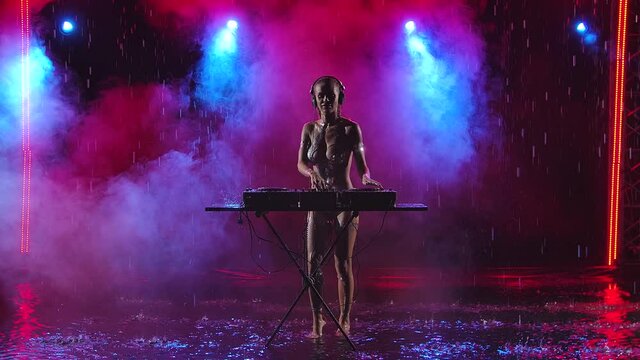 DJ hot nude female with a gorgeous slim body covered in bodypainting dancing and performing live in a dark studio under the raindrops. Slow motion.