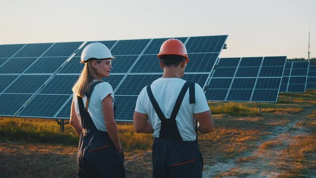 Interracial workers couple exploring photovoltaic power field with installed solar batteries using tablet computer for management. Cooperation. Solar field.