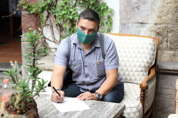 
Latino man with protection mask, sitting in waiting room reviewing and signing documents, new normal covid-19