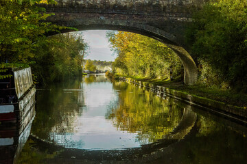 Autumn reflections of Wolfhamcote Bridge No 98, narrowboats, autumn leaves, colors, Oxford Canal near Wolverton, England.  Peaceful autumn light. Picturesque, scenic. Canal life.  Destination holiday.