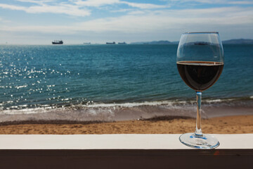 Romantic glass of wine on the white railing, sitting on the beach on the coast, red wine on the background of the sky with clouds and ship.