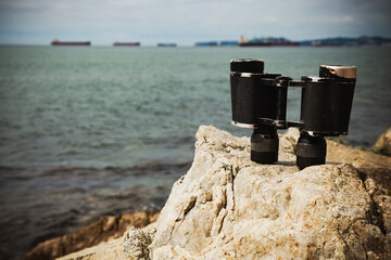 Old binoculars on the rocks of the sea coast against the background of the sea and ships standing...