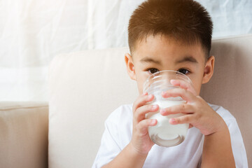Close up of happy Asian little cute child boy hand holding milk glass he drinking white milk during...