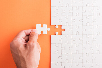 Top view flat lay of hand-holding last piece white paper jigsaw puzzle game last pieces put to...