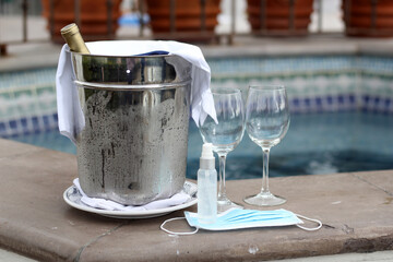 
cold wine bottle in aluminum cooler and crystal glasses with protection mask and antibacterial gel, new normal