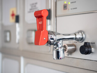shiny hot water tap with red lever in aircraft galley.