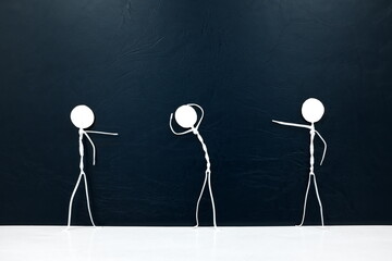 People figures pointing fingers on a scared stick man  on a dark background. Bullying, victim...