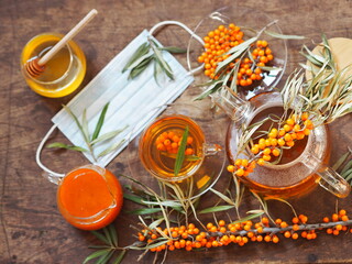 The concept of the protection and treatment of influenza with folk remedies using the beneficial sea buckthorn berries. Medical masks with sea buckthorn branches on a dark wooden table.