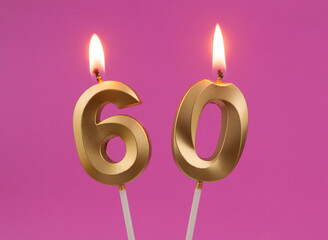 Burning golden birthday candles on pink background, number 60