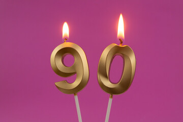 Burning golden birthday candles on pink background, number 90