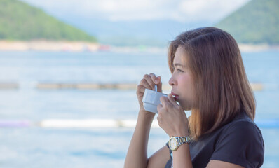 Portrait Asian woman holding a coffee cup in hand and drinking  Background Water blur and the mountains in the dam
