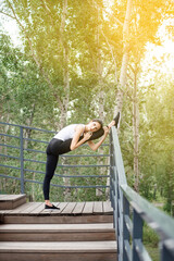 a woman stretches her leg muscles for splits in nature, against the background of a forest with sunlight