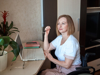 A woman freelancer, disabled in a wheelchair, works remotely from home on a laptop
