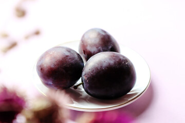 Fresh plums on a white saucer close-up, bokeh - the concept of using vitamin berries in cooking
