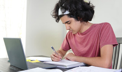 Fototapeta premium High key image of a teen boy doing remote school in times of Covid-19, taking math notes from a virtual lesson on his laptop. 