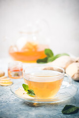 Ginger tea in a glass cup with lemon and mint on light background