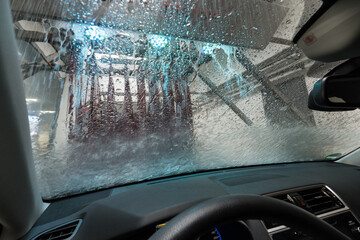 Automatic car wash with conveyor belt. A view from the car through the windshield at the rotating...