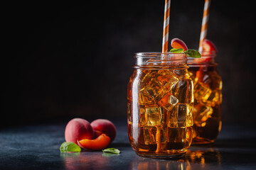 Glass of peach or apricot iced tea with fruit slices against dark blue background