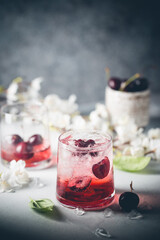 Cold cherry lemonade drink with fresh cherry and ice on gray background