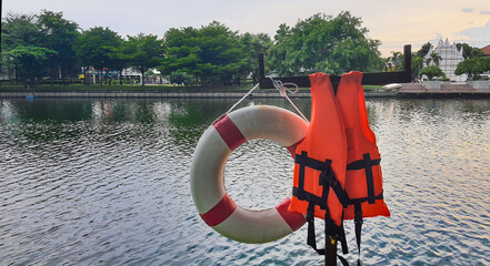orange life jacket and red and white rubber ring, safety equipment beside lake. It's useful for...