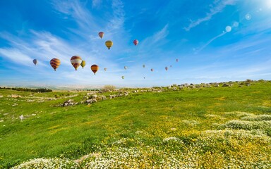 Hot air balloons fly in blue sky over green hills near Denizli, Turkey.