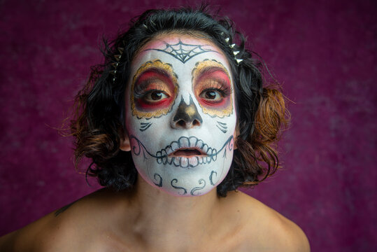 Mujer joven millennial bonita maquillaje catrina mexicana latina día de los muertos halloween calavera cara pintada festividad disfraces fondo rosa punk moderna urbana modelo expresión sorpresa mirada