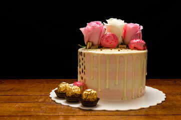 Hermoso pastel decorado con rosas naturales y chocolates, sobre mesa de madera. Hecho en casa.