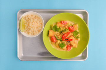 Fresh rice and chicken in gravy sauce with tomatoes, red pepper and green beans served in seperate plates on metal tray.