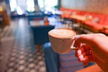 Male hand hold mug of espresso or americano coffee. Selected focus, blurred background. Inside of a restaurant or cafe.