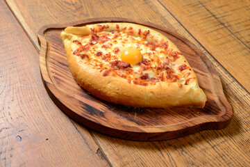 Hhachapuri with cheese and egg on a plate served on a wooden board over rustic wooden table.
