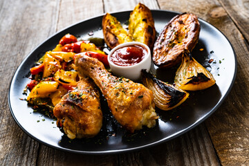 Barbecue chicken drumsticks with fried potatoes  vegetables on wooden table
