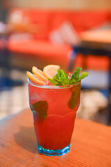 Red fruit cocktail drink with raspberry, mint and ice on dark rustic wooden table in a bar or restaurant.