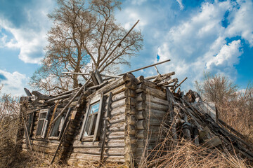 Old rustic wooden log house destroyed, without a roof against a blue sky with white clouds. Rural scene, olden time