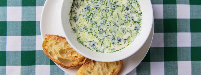 Popular spring and summer cold soup okroshka. Okroshka in a bowl, lemon and herbs on rustic wooden table.